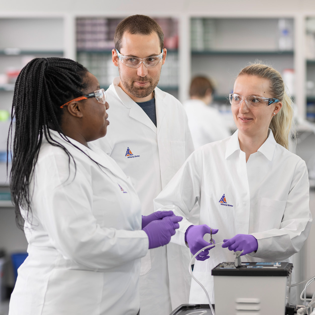 Three people in lab attire in discussion in a lab.