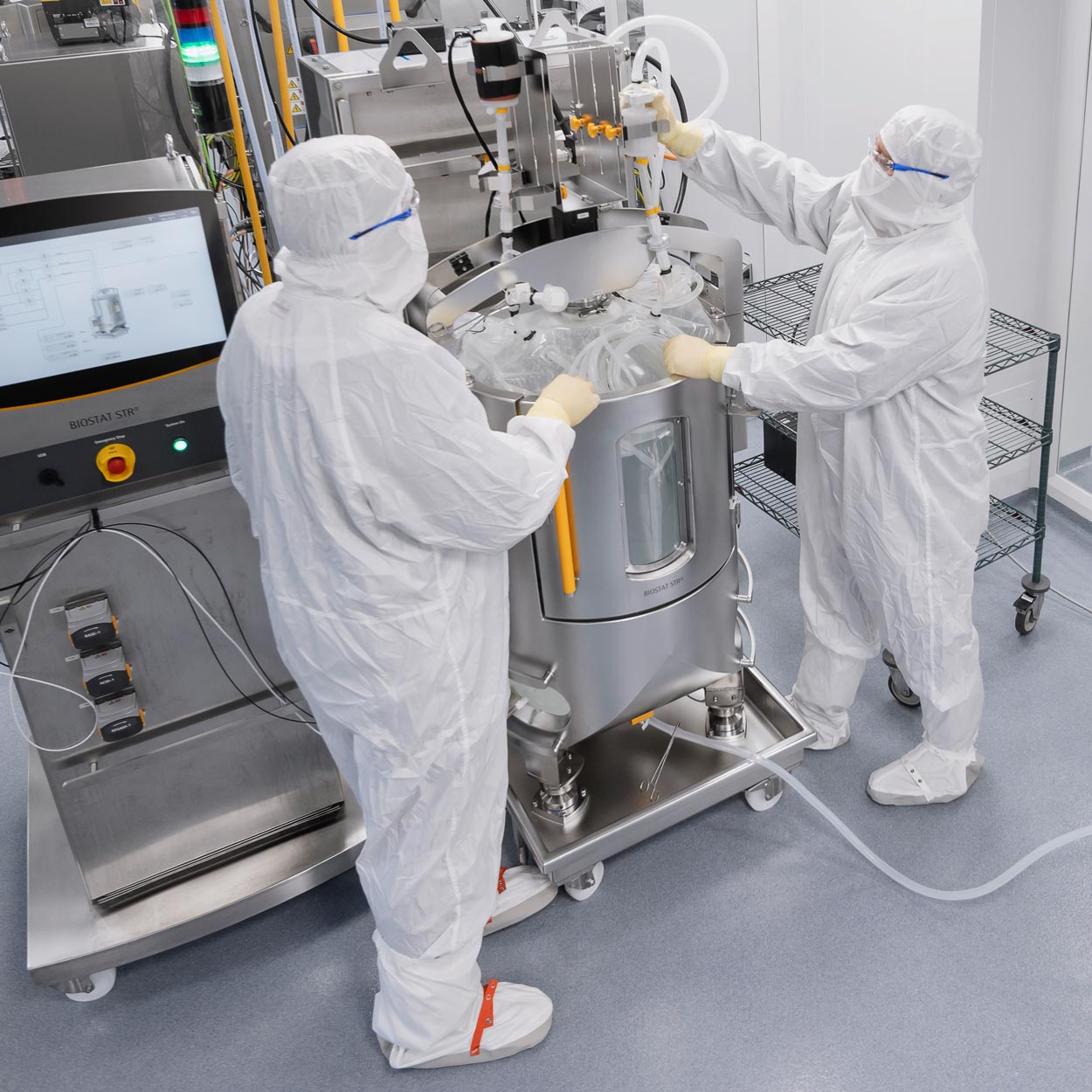 Two people in clean room attire handling a medium bioreactor.