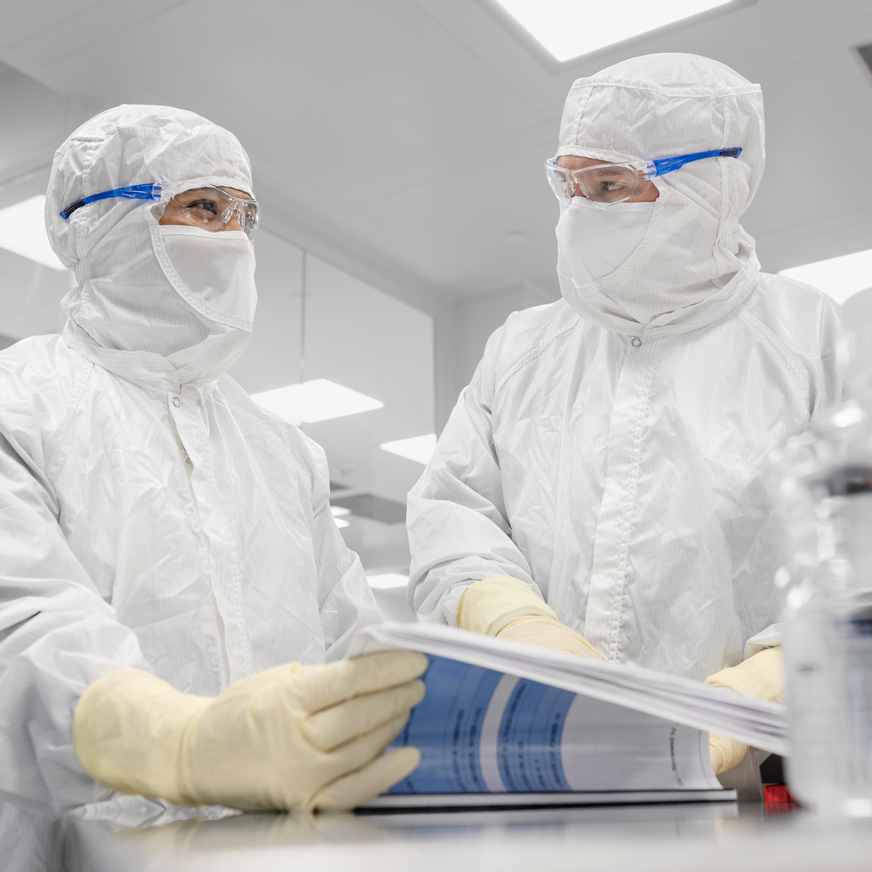 Two people in clean room attire looking over procedure sheets.