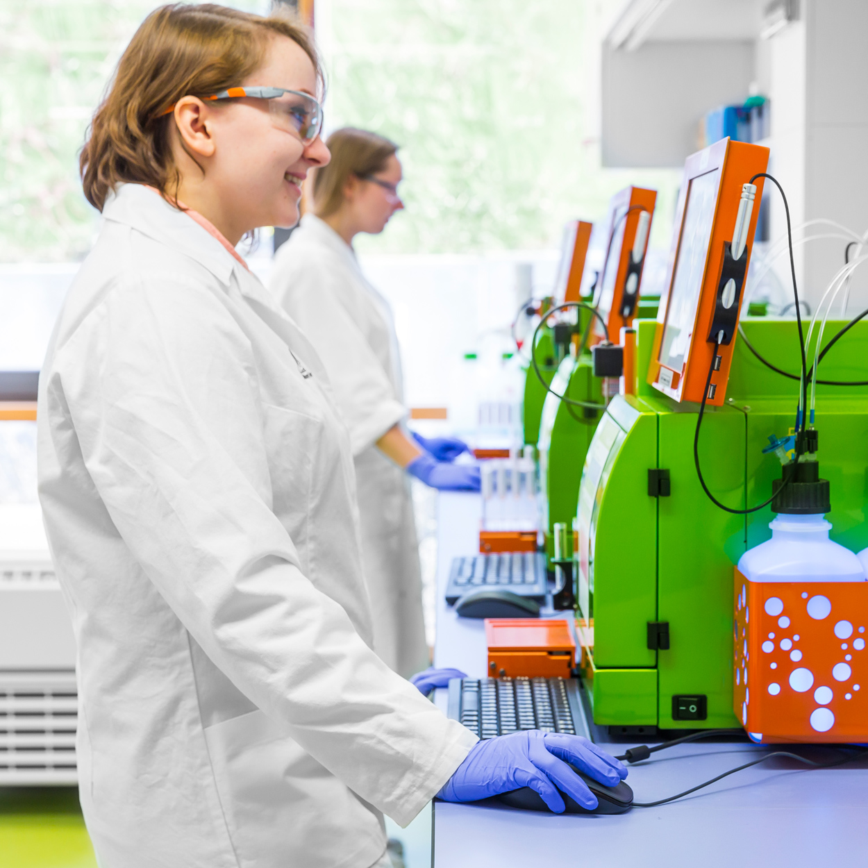 Two females wearing lab attire working on a row of MACSQuant Analyzers.